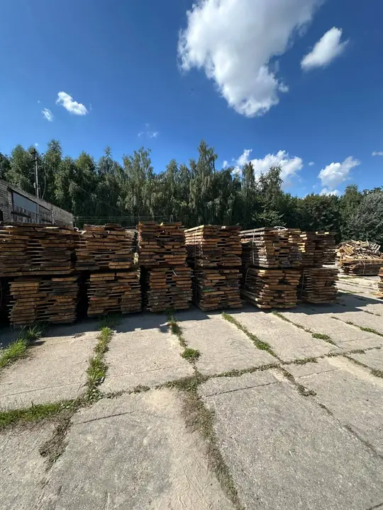 Rzędy pakietów tarcicy dębowej, w tle drzewa